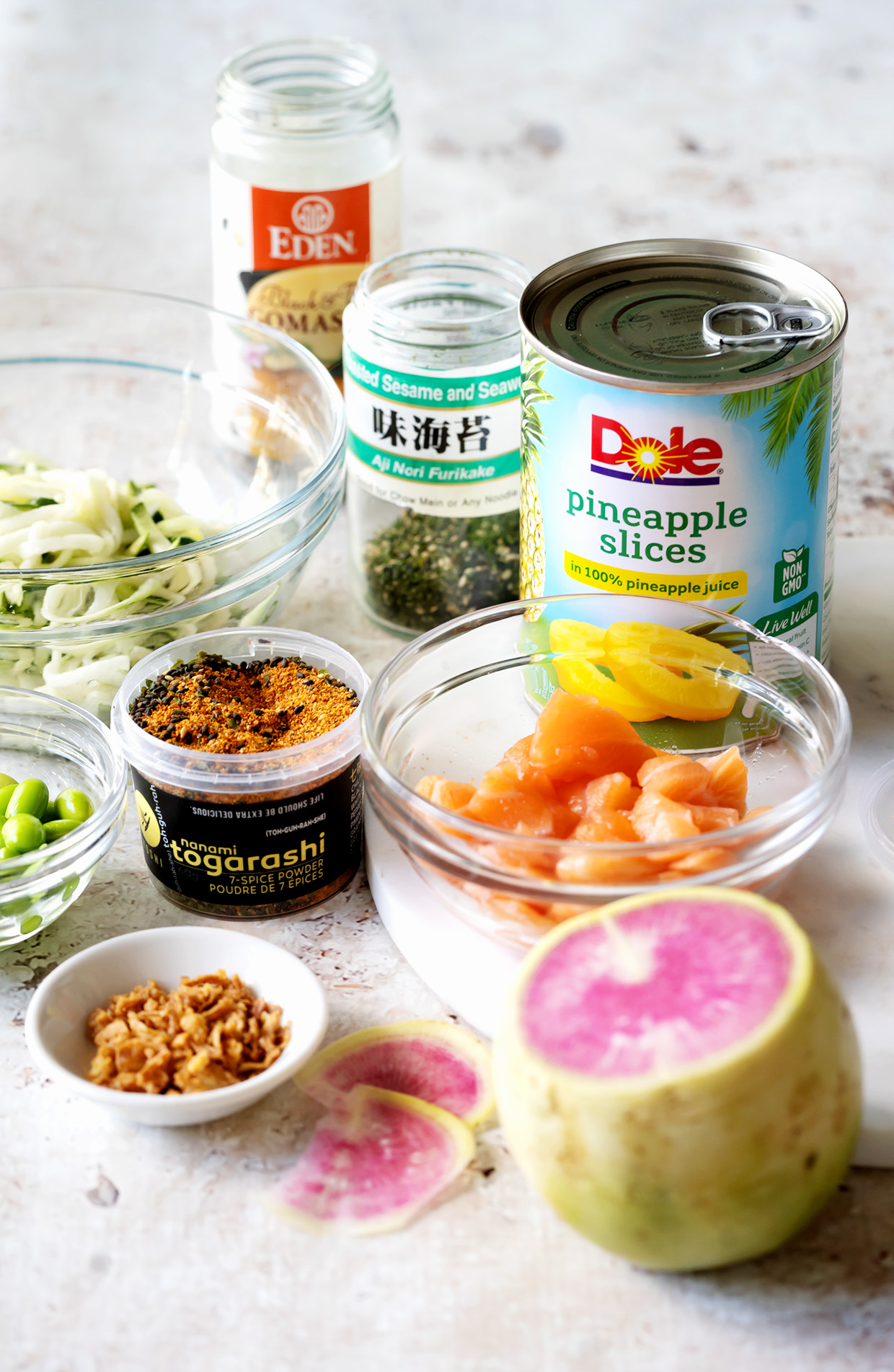 The ingredients for making a salmon bowl include, salmon, pineapple rings, zucchini noodels, edamame, Togarashi, Furikake, spicy mayo and ponzu sauce